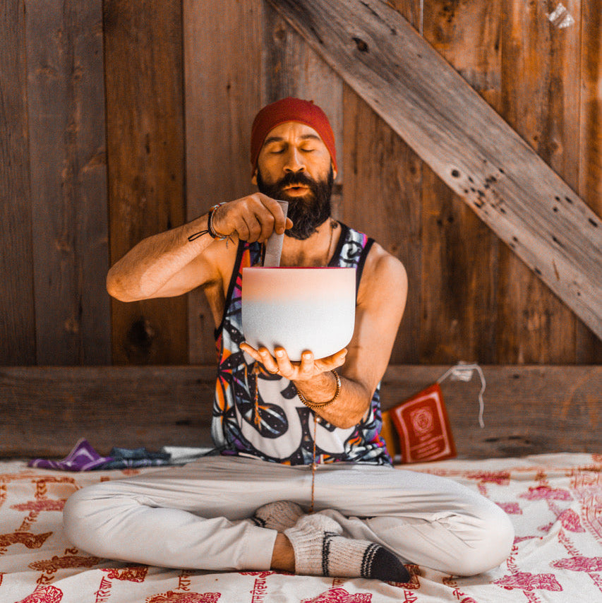 Man sitting on a rug in a wooden room holding a white bowl.